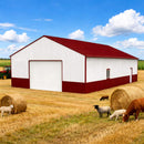 Red and white barn with sheep and hay bales in a field under a blue sky.