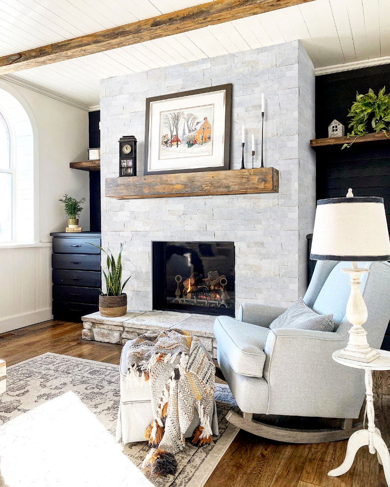 Carrara White Ledger 3D Panel 6"x24" Natural Marble Wall Tile - Full Truckload installed indoors around fireplace wooden mantel candles gray armchair and ottoman wooden floors wide view