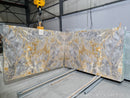 Marble slabs with gray and gold patterns on a concrete floor, with a crane in the background.