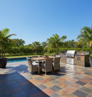 Outdoor patio with dining table, chairs, and grill area near a pool