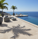 Outdoor patio area with pool, chairs, and palm trees overlooking the ocean.