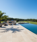 Outdoor patio area with pool, chairs, and palm trees on a sunny day.