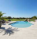 Pool area with lounge chairs, table, and palm trees on a sunny day.