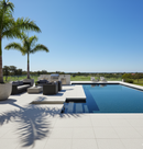 Outdoor patio area with pool, chairs, and palm trees on a clear day.