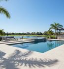 Pool area with lounge chairs, table, and palm trees under a clear blue sky.