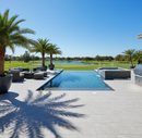 Outdoor pool area with lounge chairs, palm trees, and a clear blue sky.