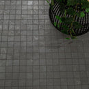 Dark gray square mosaic floor tiles with a textured stone-like finish, shown with a black wire planter containing green trailing vines in the upper right corner.