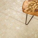 Beige mosaic tile flooring shown from an overhead angle, with a wooden chair and fluffy tan cushion partially visible in the top-right corner.
