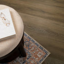 Round ottoman with a book and glasses on top, next to a small decorative rug on a wooden floor.