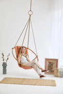 bresse rast blue hanging round chair teak frame woman sitting blue vase decorative throw blanket wicker rug on floor