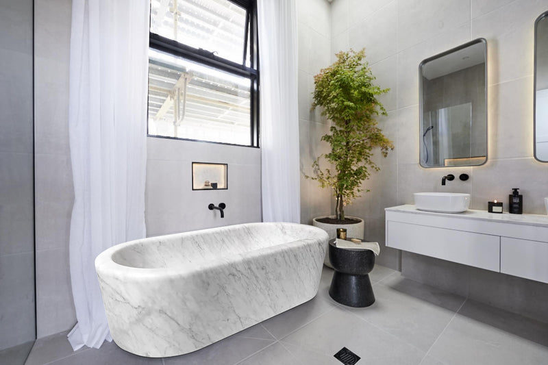 Imperial White Marble Bathtub Hand-carved from Solid Marble Block (W)32" (L)70" (H)20"installed high ceiling bathroom big black windows and a tree inside a big vase gray ceramic floors wide view