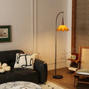 Curved black floor lamp with amber petal shade and living room shelf