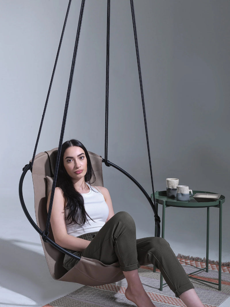 Faux Leather Round Hanging Chair Mink a woman sitting on and green side table next to her wide view