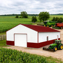White barn with red roof in a rural setting with green fields and farm equipment.