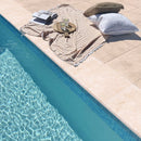 Miletos Ivory 12"x24" Tumbled Travertine Pool Coping - Full Truckload peshtemal pillows on top 2 glasses of drink and a boo next to swimming pool