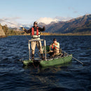Two people on a green fishing float tube in a lake with mountains in the background