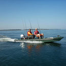 Two people on a green inflatable boat with fishing rods, speeding across calm water.