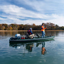 Two people fishing from a boat on a calm lake with trees in the background