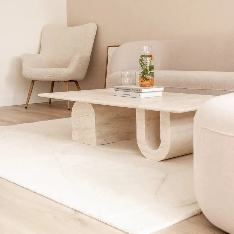 Troia Light Travertine Designer Coffee Table U Shape Legs (W)28" (L)48" (H)13" installed living room white area rug on floor beige walls magazines on the coffee table spa water inside glass bottle and 2 glasses closeup