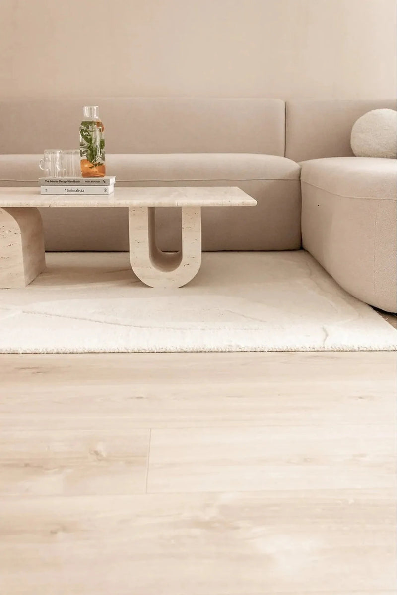 Troia Light Travertine Designer Coffee Table U Shape Legs (W)28" (L)48" (H)13" installed living room white area rug on floor beige walls magazines on the coffee table spa water inside glass bottle and 2 glasses side view