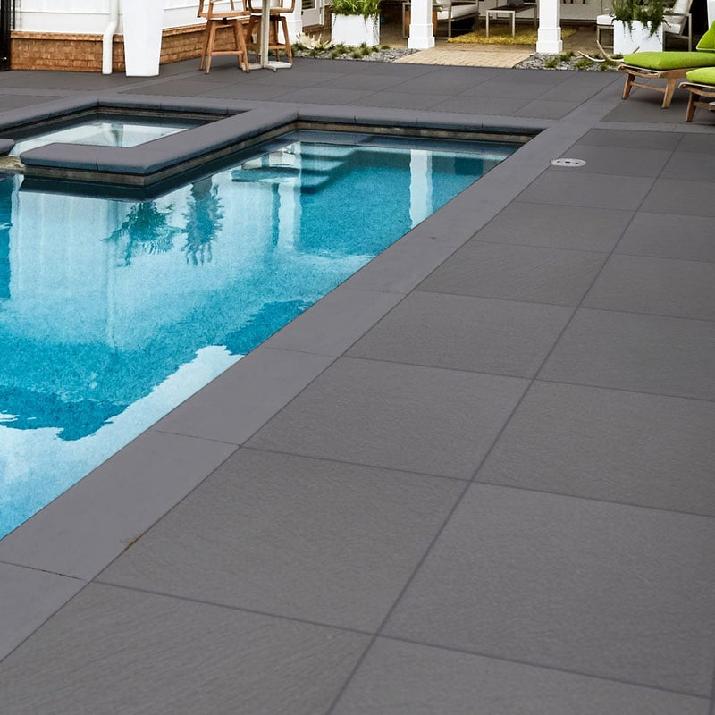 blue stone porcelain pavers 24x24in matte floor tile LPAVNBLUSTO2424 installed around swimming pool on backyard of a nice house closeup