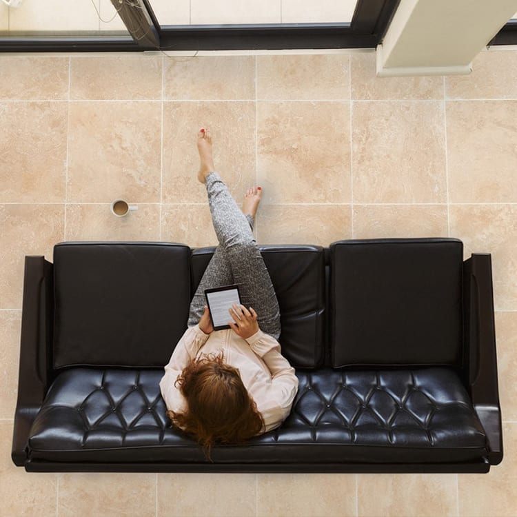 light beige premium travertine tile 24x24 Honed Filled woman sitting on black sofa reading ebook